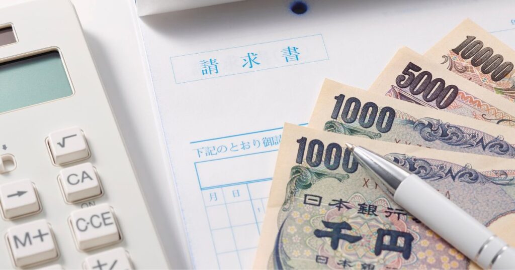 請求書と電卓の横に日本円とペンが置かれている様子